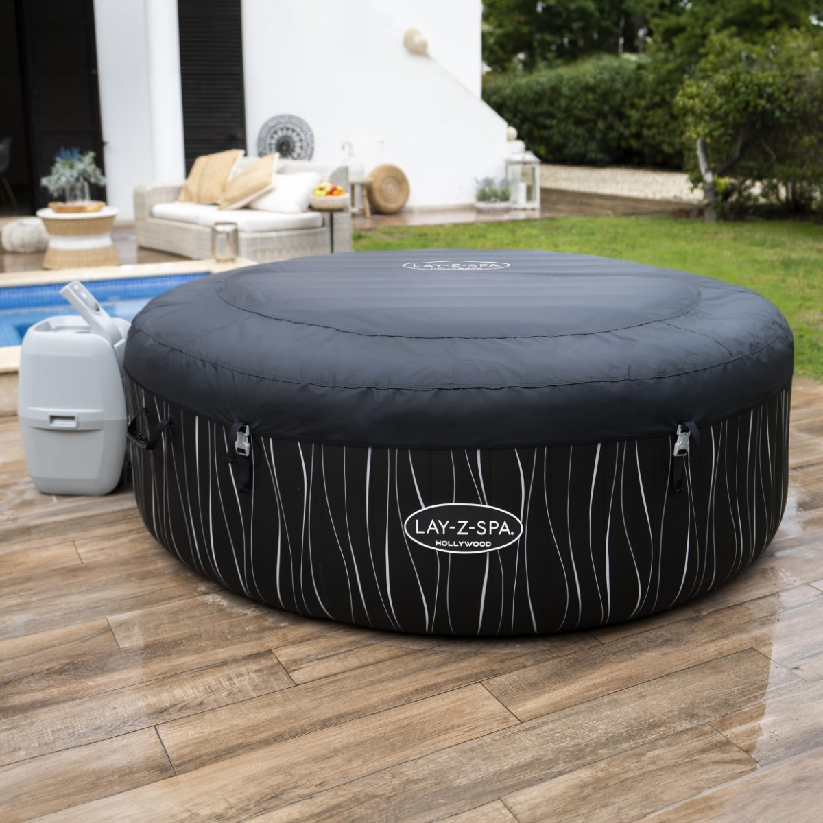 Jacuzzi z nałożoną ciemnoszarą, wzmocnioną pokrywą zabezpieczoną klamrami. Produkt stoi na zielonym trawniku obok nowoczesnego domu z basenem.